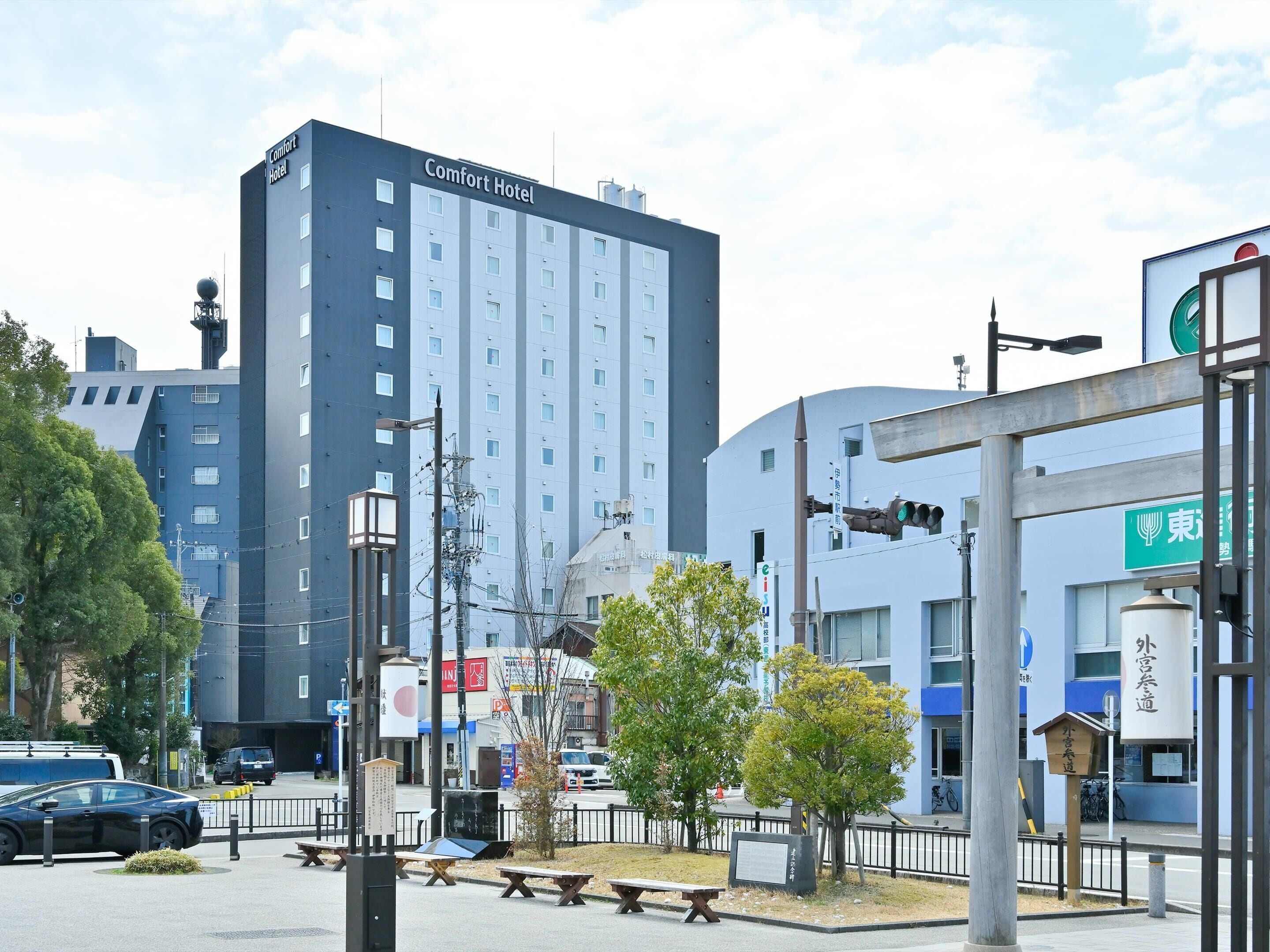 A modern Comfort Hotel with a prominent sign, located in an urban setting with surrounding buildings and a street with parked cars.