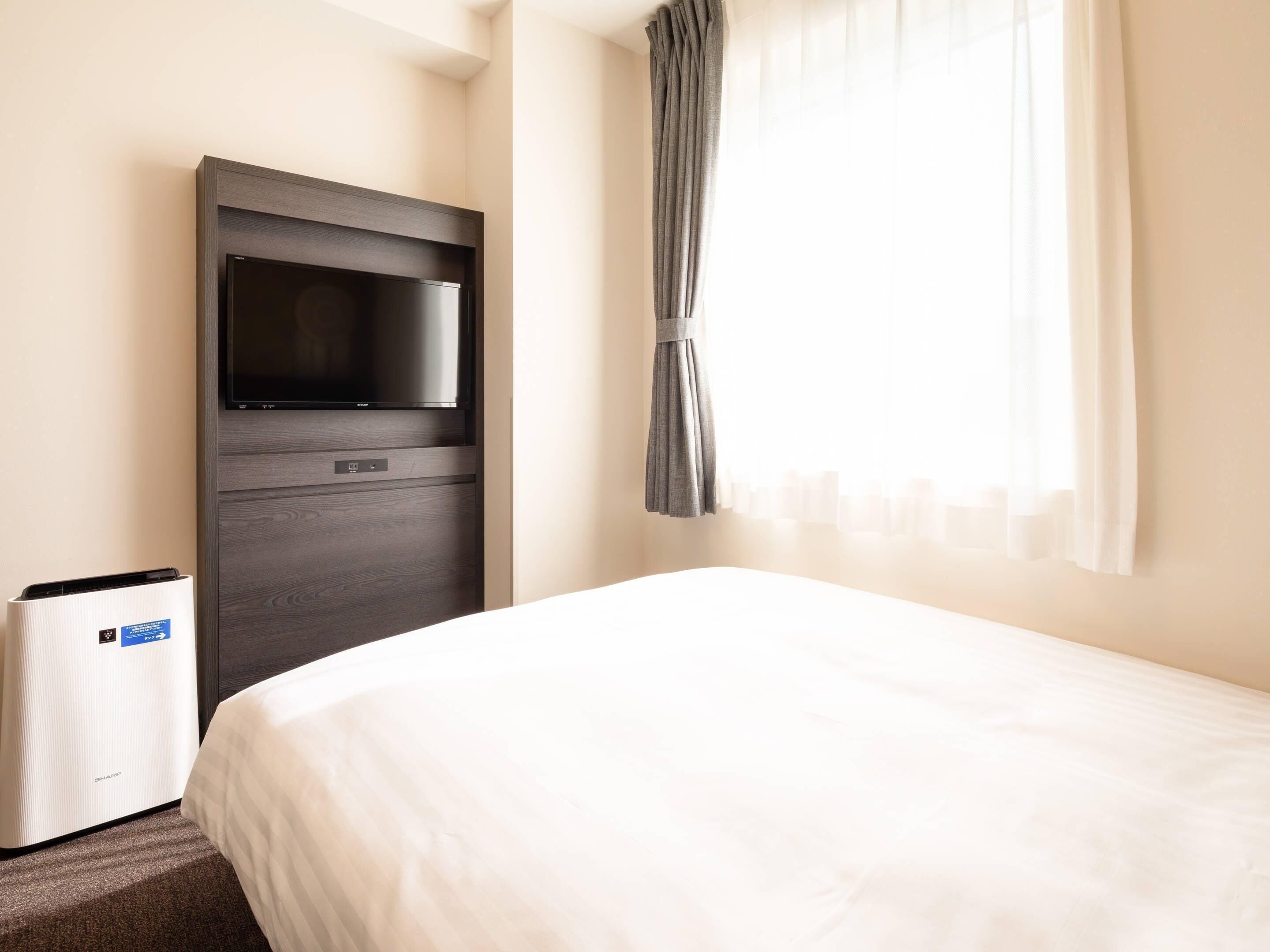 Una habitación de hotel con cama, televisión y purificador de aire integrado en la pared.