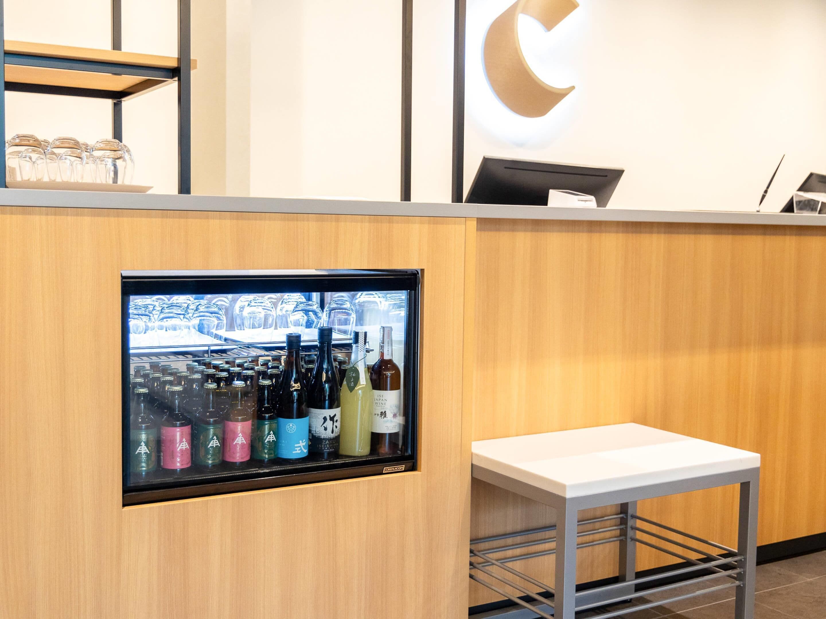 A reception area with a wooden counter, a glass display case with bottles, and a white table.