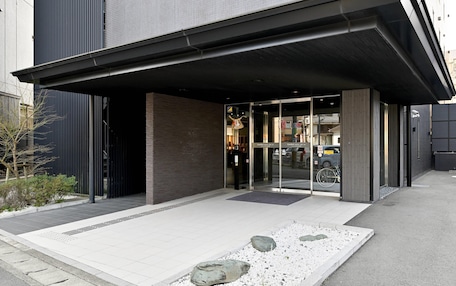A modern hotel entrance with a covered walkway, glass doors, and a small garden area with rocks.