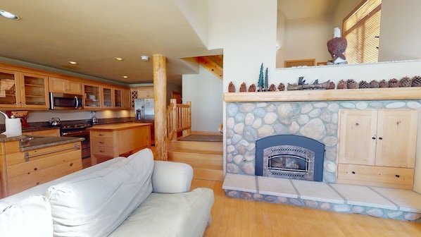 A modern kitchen with wooden cabinets, a built-in microwave, and a stone fireplace with a mantel. - Snowcreek Resort Vacation Rental 719 (Mammoth Lakes)