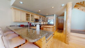 Una cocina con encimeras de granito, armarios de madera, un lavamanos de acero inoxidable y un microondas integrado.