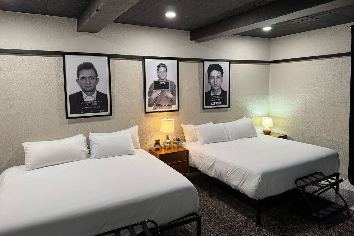 Une chambre d’hôtel avec deux lits, une table de chevet avec une lampe et trois affiches encadrées au mur.