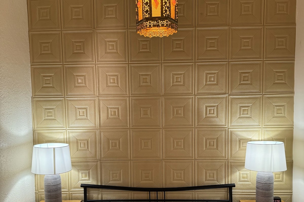 Une chambre d’hôtel avec un grand lit, deux tables de chevet, un panneau décoratif au mur et un luminaire suspendu.