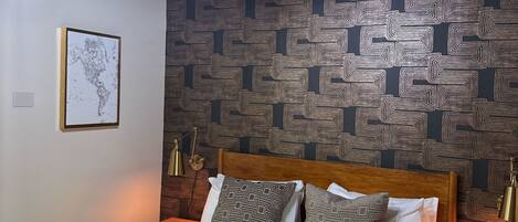 A bedroom with a patterned wallpaper, a wooden headboard, a bed with patterned bedding, and a wall-mounted globe.