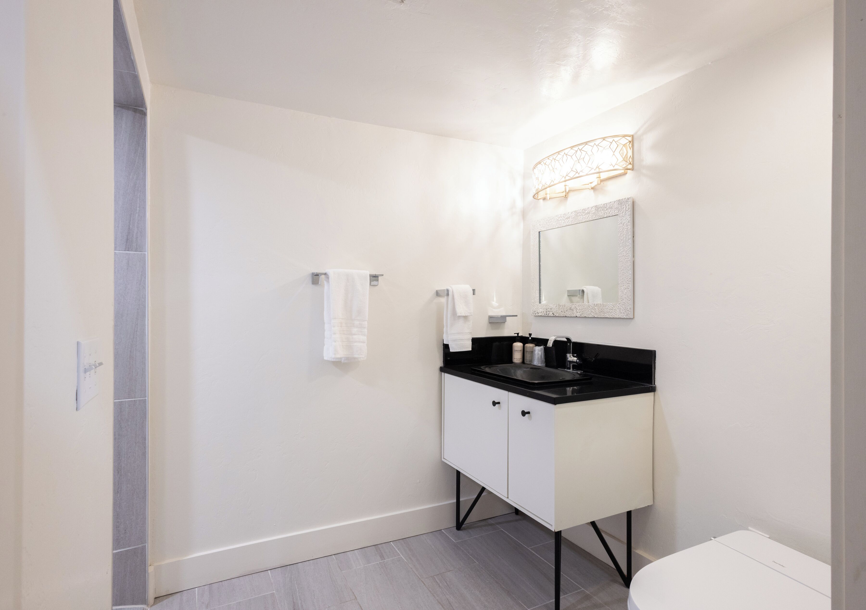 A modern bathroom with a white sink, black countertop, and a large mirror.
