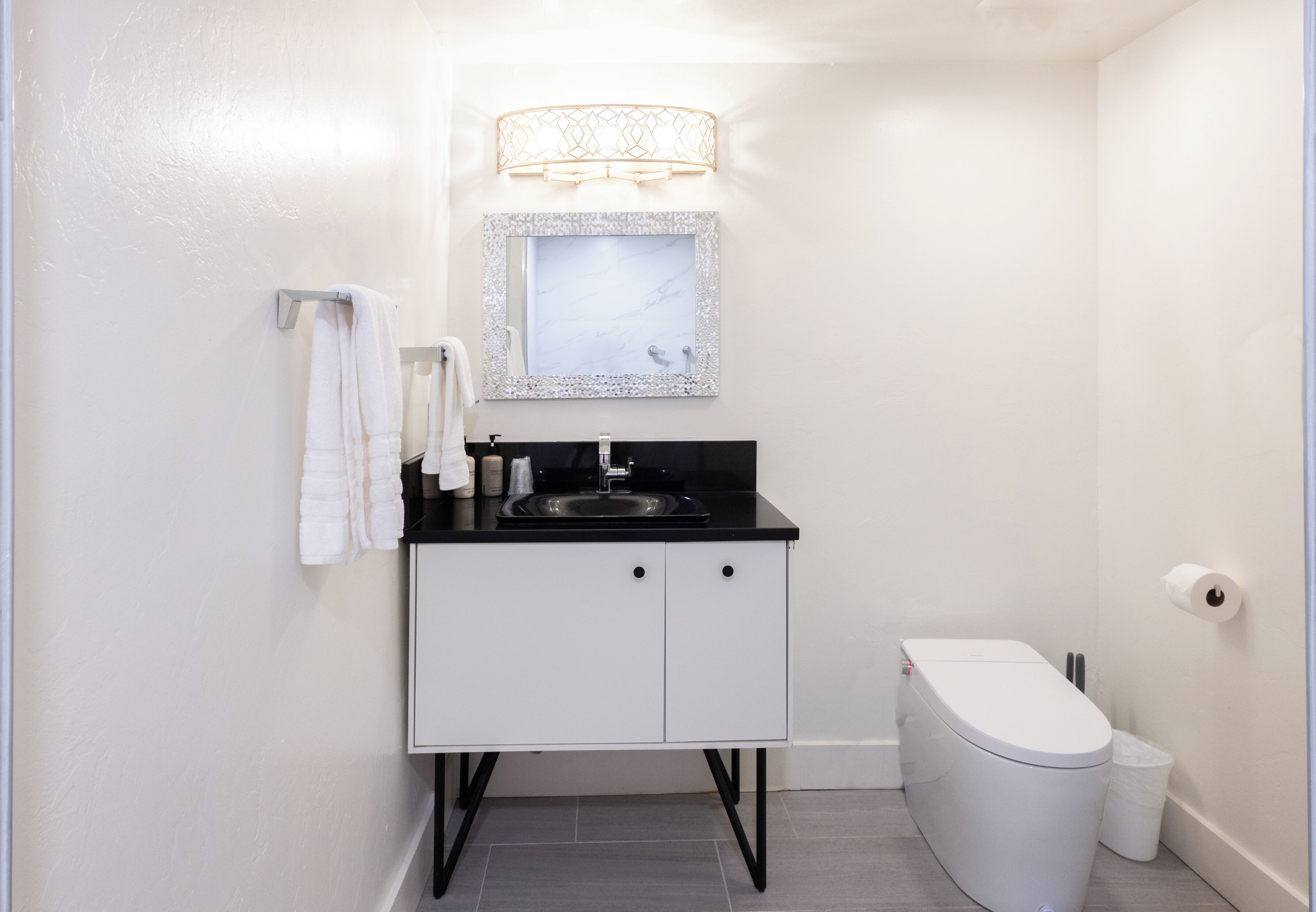 A compact bathroom with a white sink, black countertop, and a white toilet. There is a mirror with a decorative frame above the sink.