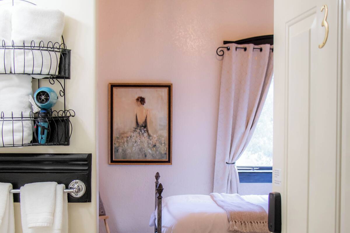 Une chambre à coucher avec un lit, un tableau au mur, une fenêtre avec des rideaux et une porte.