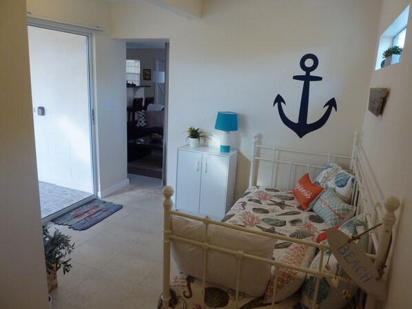 Un dormitorio con cama, un armario blanco, una puerta que da a otra habitación y una pared decorada con un ancla.