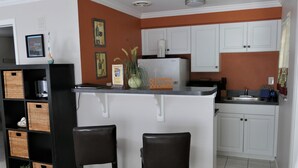 A compact kitchen with white cabinets, a small island with two stools, and a refrigerator. - Sun, beach, and great savings –discover amazing discounts on dream destinations! (Cape Coral)