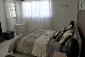 Een slaapkamer met een bed, een dressoir, een raam met gordijnen en een bord aan de muur.