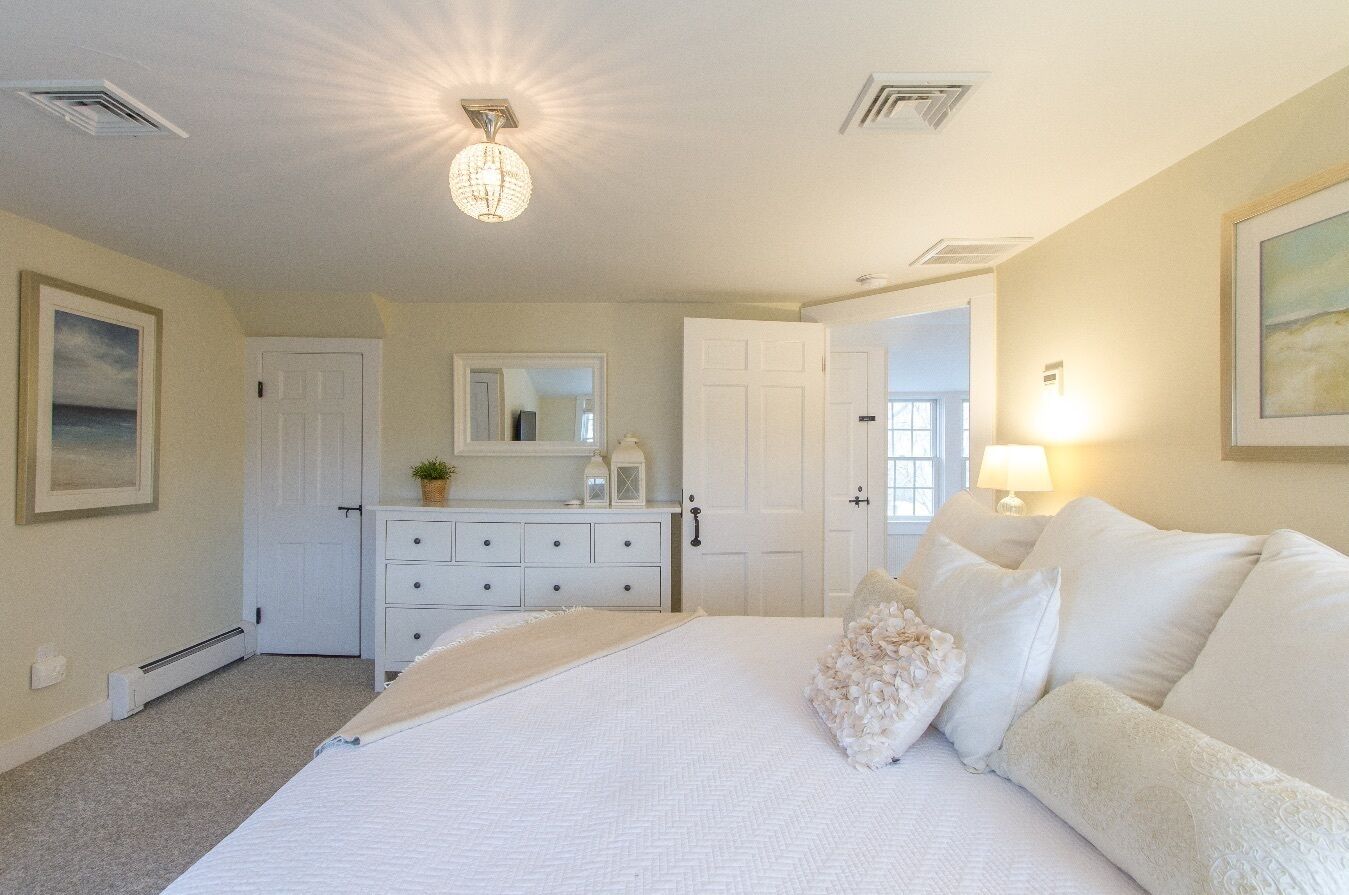 A bedroom with a large bed, a dresser, a mirror, and a door leading to another room.