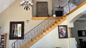 A spacious living room with a wooden staircase, a chandelier, and a large mirror.