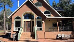 A two-story house with a brown exterior, large windows, and a covered porch with outdoor seating.