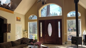 A spacious living room with a high ceiling, large windows, a fireplace, and a cozy seating area.