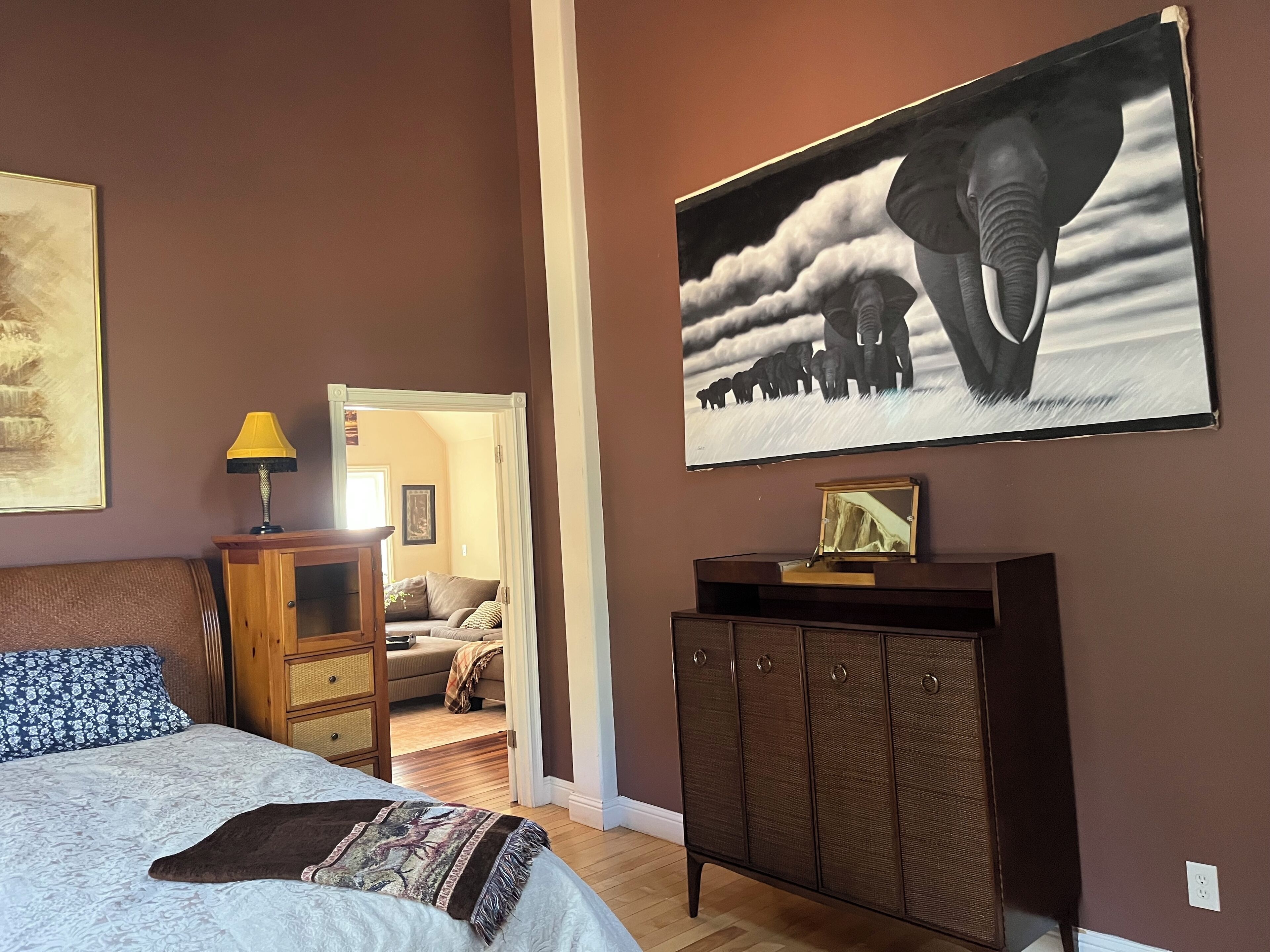 A bedroom with a bed, a nightstand, a dresser, and a large framed picture of elephants.
