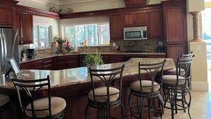 A spacious kitchen with dark wooden cabinets, a granite countertop, a stainless steel refrigerator, a microwave, and a large island with bar stools.