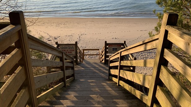 Eine Holztreppe führt zu einem Strand, an dem ein Schild vor Strömungen warnt.