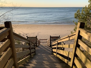 Una escalera de madera que lleva a una playa, con un cartel de advertencia sobre corrientes de resaca.