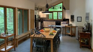Eine moderne Küche mit großen Fenstern, einem Essbereich mit Holztisch und -stühlen sowie einer Kücheninsel mit Spüle und Arbeitsfläche.