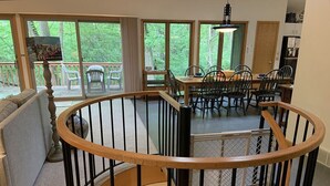 Ein Essbereich mit Holztisch und -stühlen, eine Treppe mit hölzernem Geländer und große Fenster mit Blick auf Grünflächen.