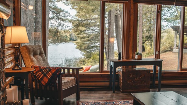 Una habitación acogedora con un ventanal grande, una silla de madera, una mesita y una alfombra.