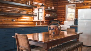 Cocina de cabaña de madera con mesa de comedor, sillas, un cesto de aperitivos y un refrigerador.
