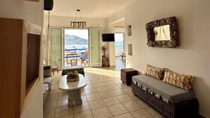 A spacious living area with a sofa, a coffee table, and a view of the sea through a glass door. - Paros Dream House #Naoussa Parodise (Naousa)
