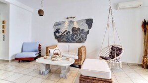 A modern living room with a white sofa, a wicker chair, a hanging macrame chair, a marble coffee table, and a decorative wall piece. - Paros Dream House #Naoussa Parodise (Naousa)