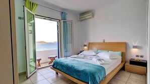 A bedroom with a bed, a nightstand, a window with a view of the sea, and a sliding door to a balcony. - Paros Dream House #Naoussa Parodise (Naousa)