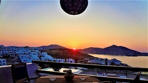 Ein Balkon mit Blick auf eine Küstenstadt bei Sonnenuntergang, mit weißen Gebäuden und einem Berg im Hintergrund.