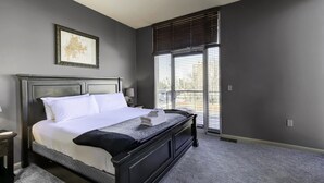 A neatly made bed with white linens and a folded towel, a dark wooden headboard, a framed map on the wall, and a window with blinds.