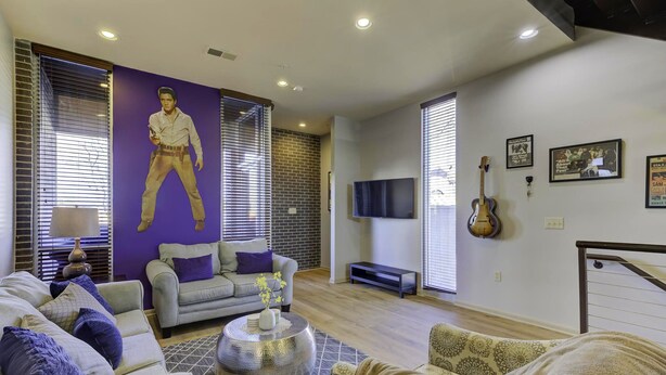 A living room with a large Elvis Presley statue, a grey sofa, a patterned rug, and a TV on the wall.