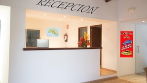 A reception area with a sign reading "RECEPCION," a map on the wall, a laptop on the counter, and a "RENT A CAR LOW COST" poster. - Binibeca Mar (Sant Lluis)