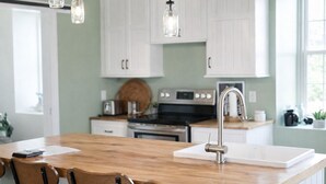 Una cocina con armarios blancos, una isla de madera con un lavamanos y lámparas colgantes.