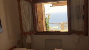 A bedroom with a bed, a window with curtains, and a view of the sea. - Villa 2 apartments ,1 or 2 families, panoramic sea view & sunset (Sinnai)