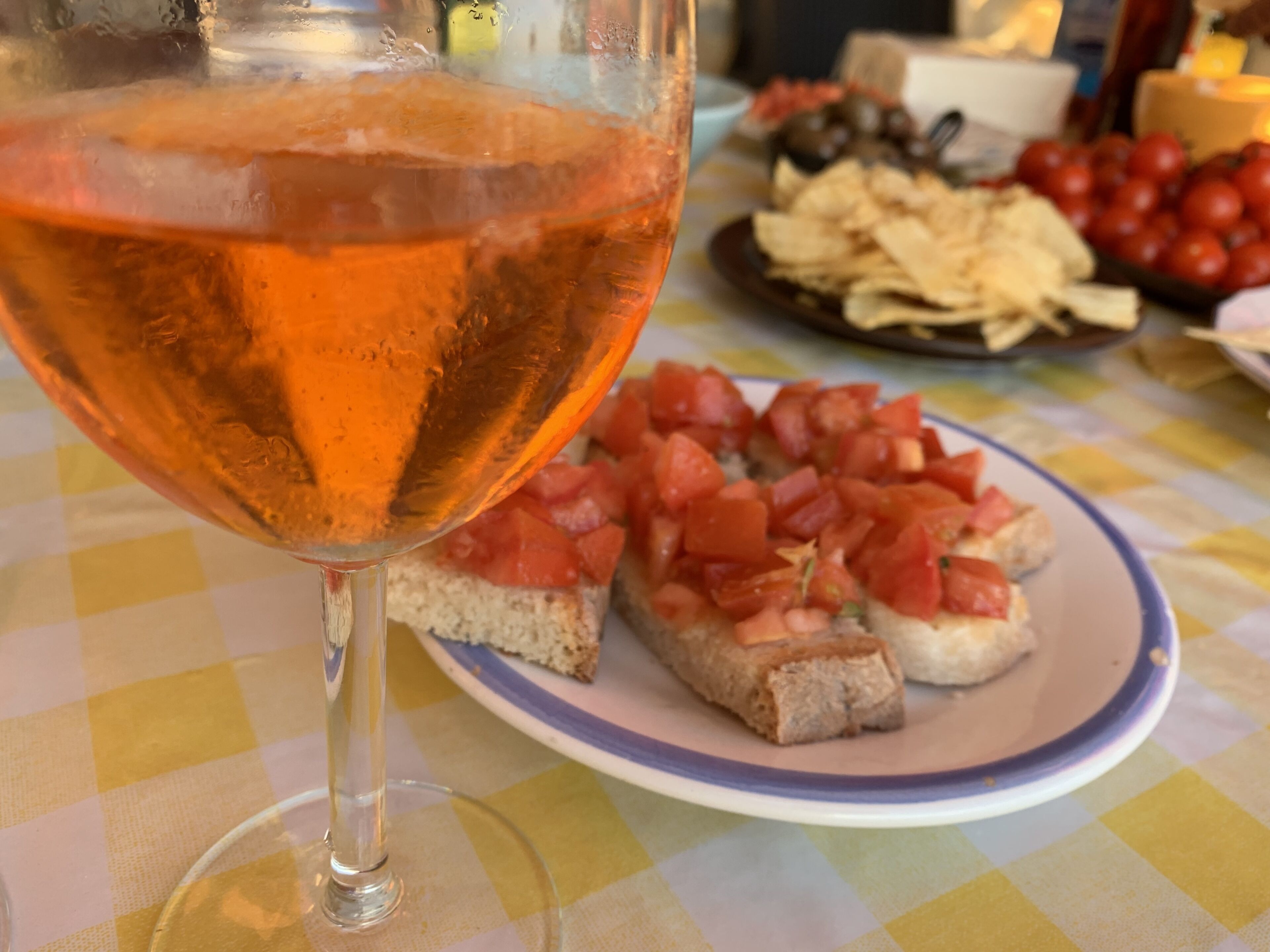 Un verre de vin rosé, une assiette de tranches de tomates et un bol d’olives sur une nappe à carreaux.