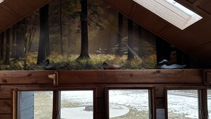 Ein Zimmer mit einem Waldgemälde an der Decke, großen Fenstern und Blick auf eine verschneite Landschaft.