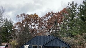 Ein Haus mit dunkelblauer Fassade, einem großen Vorgarten und einer kleinen, runden Feuerstelle.