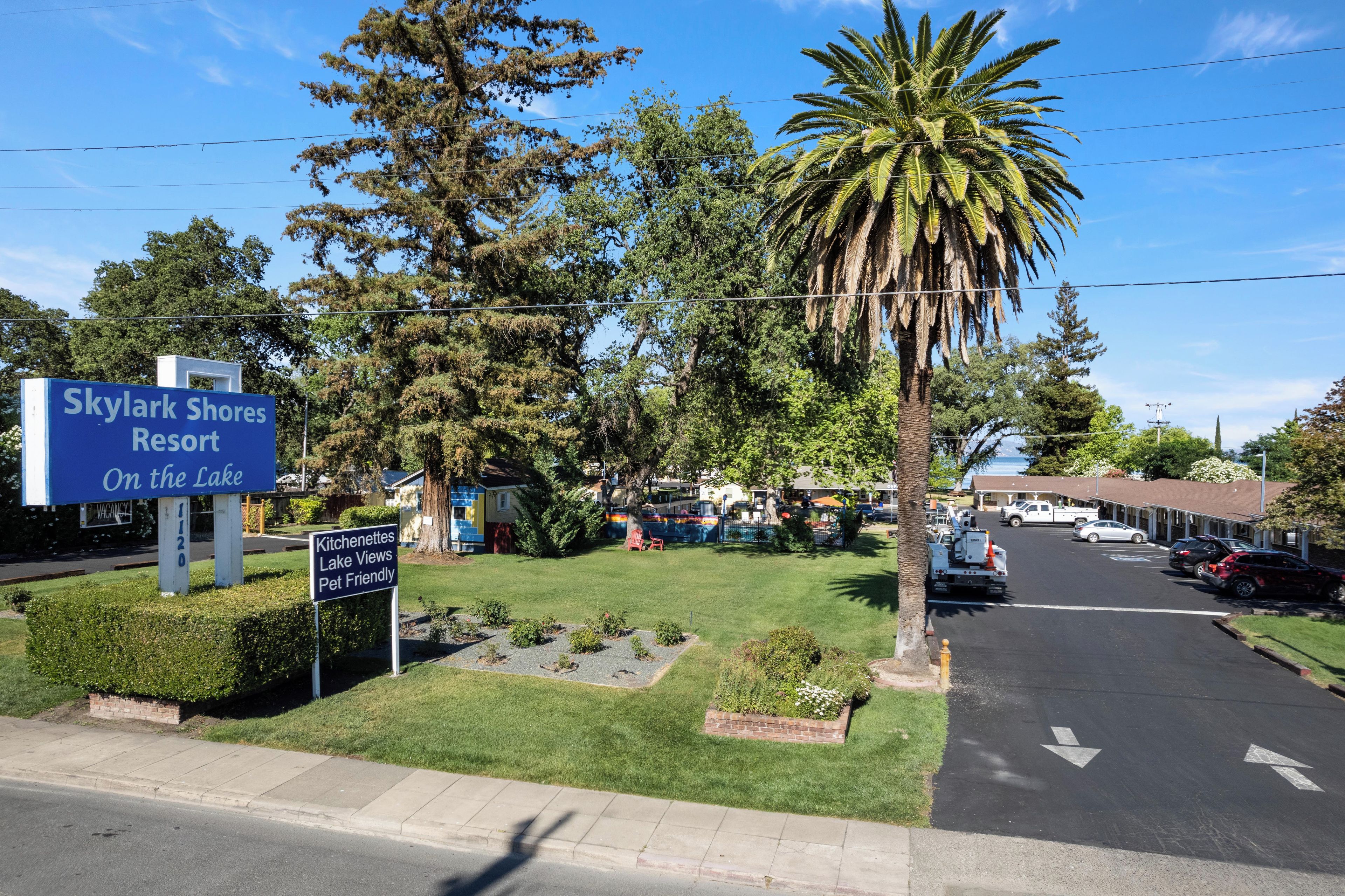 Bordje voor Skylark Shores Resort met uitzicht op de parkeerplaats en de omliggende begroeiing.