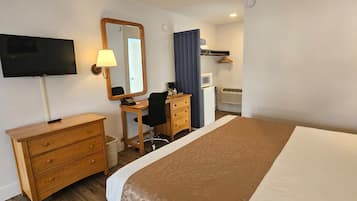 Ein Hotelzimmer mit einem Bett, einem Schreibtisch mit Stuhl, einem Fernseher, einem Spiegel, einer Kommode und einer Mikrowelle.