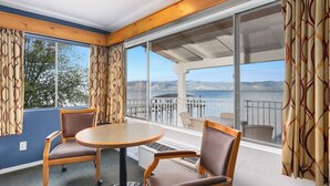 A room with a round table and two chairs, large windows with curtains, and a view of the sea and mountains. - Skylark Shores Resort (Lakeport)