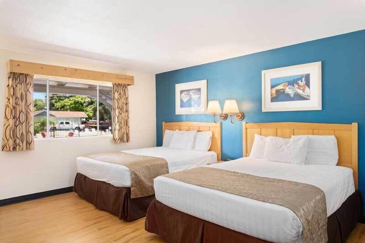Habitación de hotel con dos camas, una ventana con cortinas y dos lámparas fijadas a la pared.
