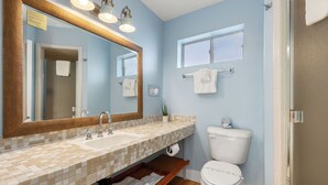 A bathroom with a tiled sink, a large mirror, a toilet, and a window. - Skylark Shores Resort (Lakeport)