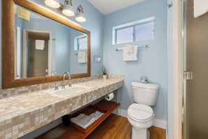 Un baño con lavamanos de azulejos, un espejo grande, un inodoro y una ventana.