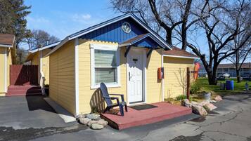 A small yellow building with a blue roof, a white door, and a blue chair outside.