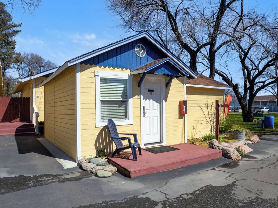 A small yellow building with a blue roof, a white door, and a blue chair outside.
