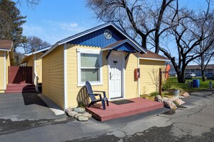 Un pequeño edificio amarillo con techo azul, una puerta blanca y una silla azul afuera.