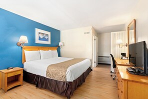 Une chambre d’hôtel comprenant un lit, des tables de chevet, un bureau avec un ordinateur, une télévision et un miroir.