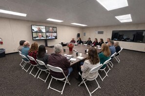 A conference room with a large table, chairs, a screen displaying multiple video feeds, and a potted plant. - Skylark Shores Resort (Lakeport)